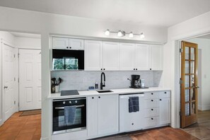 A modern kitchen with white cabinetry, a built-in oven, a coffee maker, and a window above the sink. - Cozy Condo by Downtown (Bend)