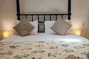 Ein Bett mit einem blumigen Überwurf, zwei Kissen mit einem geometrischen Muster und ein schwarzes Kopfteil.