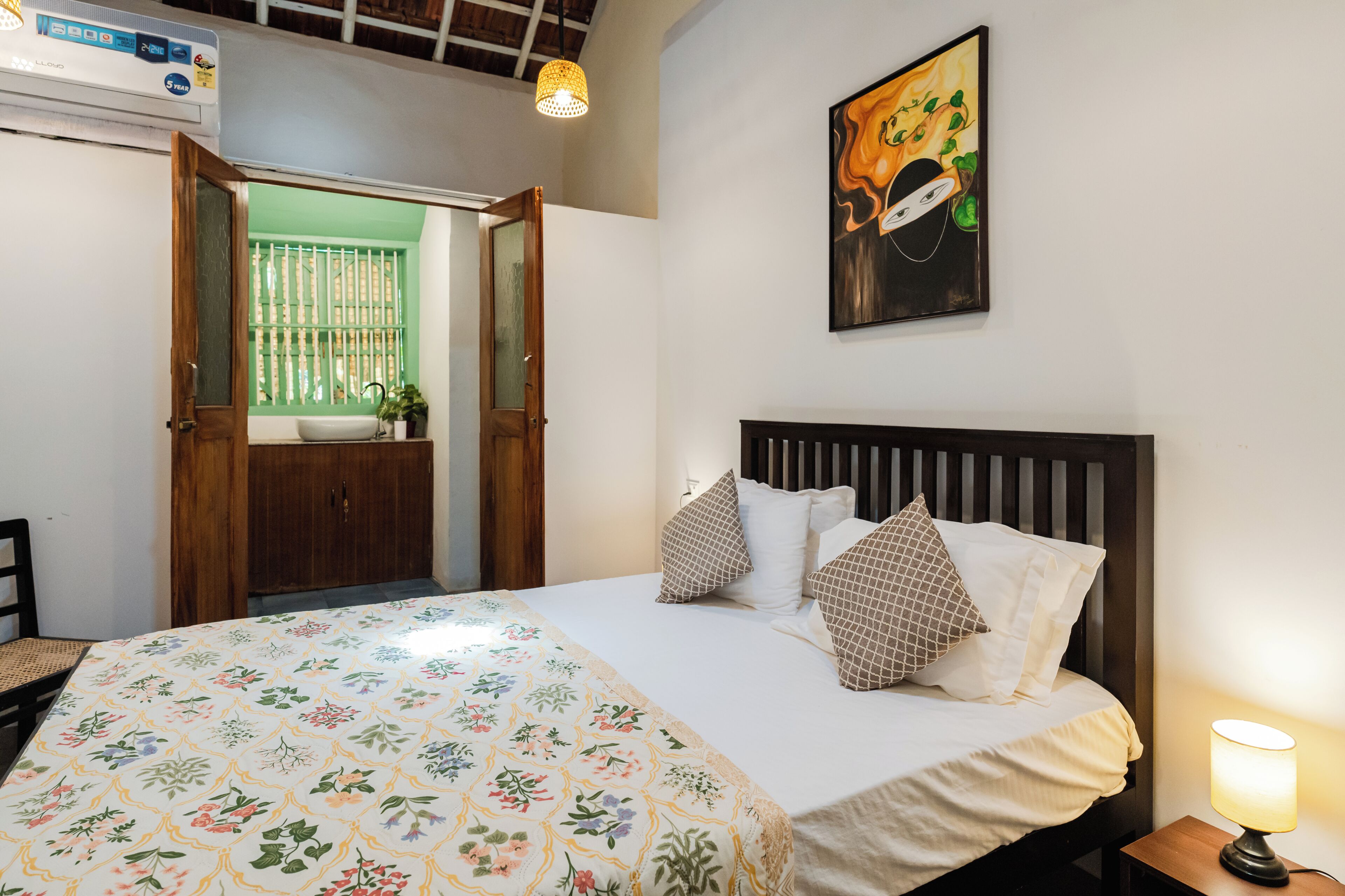 A hotel room with a bed, a bedside table, a lamp, a window with a view, and a door leading to another room.