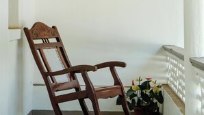 A rocking chair on a balcony with a white railing and a potted plant with flowers. - Casa Particular in Cansaulim, India (Arossim)