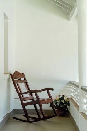 Ein Schaukelstuhl auf einem Balkon mit weißer Reling und einem Blumentopf mit Blumen.