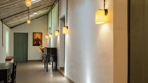 A hallway with a wooden floor, a dining table with chairs, a vase of flowers, and wall-mounted lamps. - Casa Particular in Cansaulim, India (Arossim)
