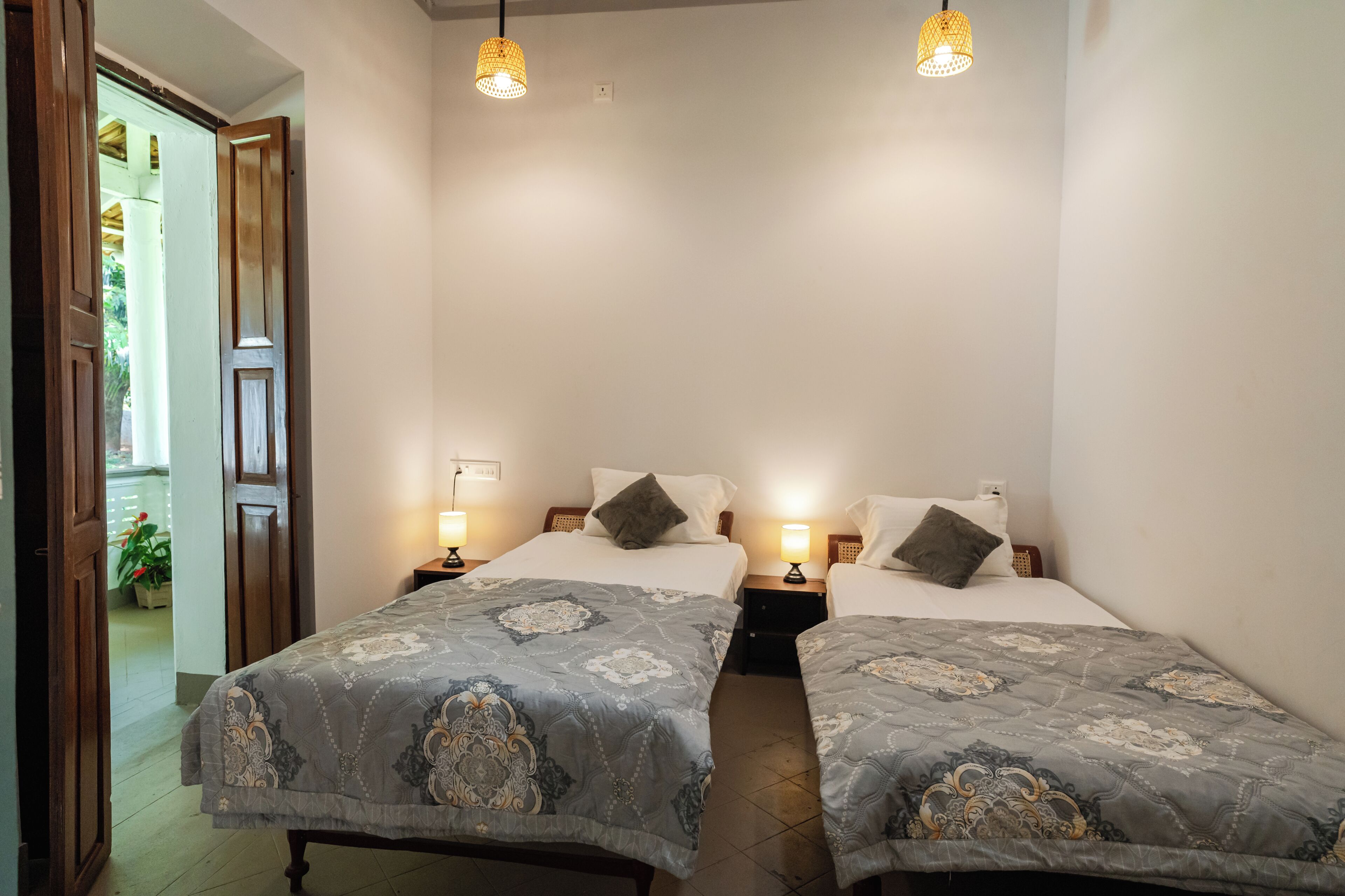 Une chambre d’hôtel avec deux lits, chacun recouvert d’une couvre-lit à motifs, dotée de lampes de chevet et offrant une vue sur une porte en bois donnant sur l’extérieur.