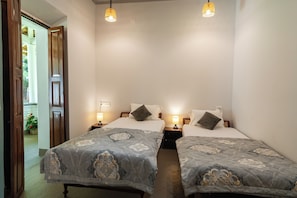 A hotel room with two beds, each with a patterned bedspread, bedside lamps, and a view of a wooden door leading outside.