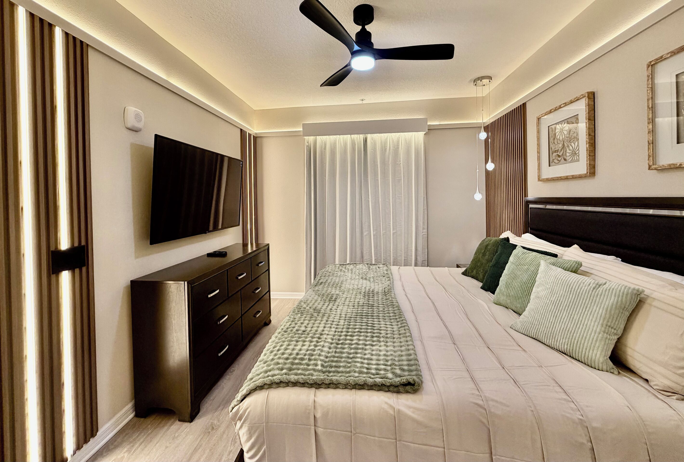 Ein Hotelzimmer mit Bett, Fernseher, Kommode und Deckenventilator.