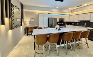 A modern kitchen with a central island, white cabinets, and a dining area with brown chairs. - 401 - Beyond the Sea & Into the Stars (Kissimmee)