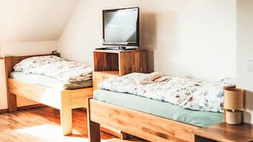 Une chambre avec deux lits superposés en bois, un téléviseur posé sur un meuble en bois et une table de chevet avec une lampe.