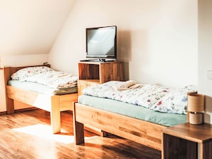 Une chambre avec deux lits superposés en bois, un téléviseur posé sur un meuble en bois et une table de chevet avec une lampe.