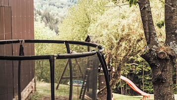 Ein Trampolin mit Sicherheitsnetz, umgeben von Bäumen und einer hölzernen Bank in einem Garten.