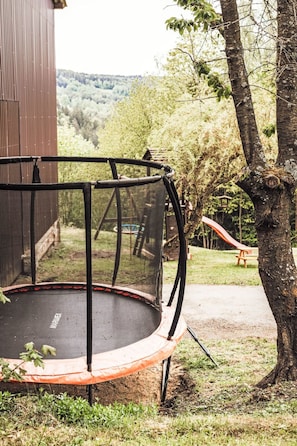 Un trampoline doté d’un filet de sécurité, entouré d’arbres et agrémenté d’un banc en bois, dans un jardin.