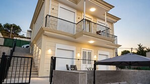 Ein zweistöckiges Haus mit Balkon, Außenbereich mit Sitzgelegenheit und einer Treppe zum Eingang.