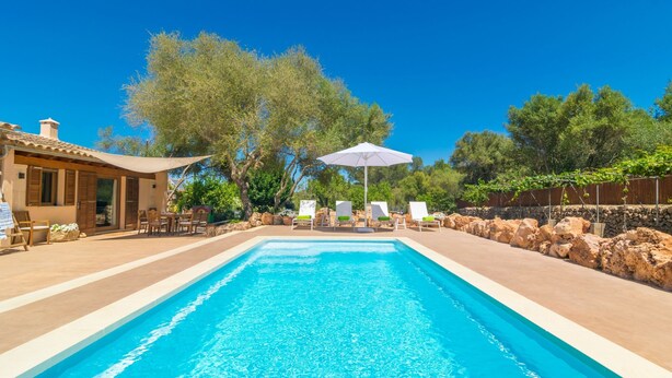 A swimming pool with lounge chairs and a table, surrounded by a stone wall and trees. - Es Tancat Prim - Villa With Private Pool (Algaida)
