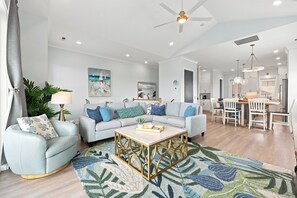A modern living room with a sofa set, a coffee table, and a dining area with chairs. - Shore Perfection | Family Beach Retreat, Sleeps 8 (Emerald Isle)