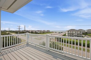 A wooden deck with a white railing overlooking a residential area with houses and a road. - Shore Perfection | Family Beach Retreat, Sleeps 8 (Emerald Isle)