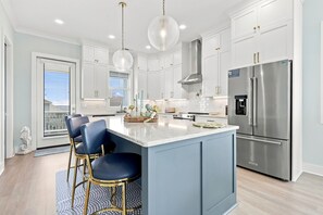A modern kitchen with white cabinets, a stainless steel refrigerator, and a central island with bar stools. - Shore Perfection | Family Beach Retreat, Sleeps 8 (Emerald Isle)