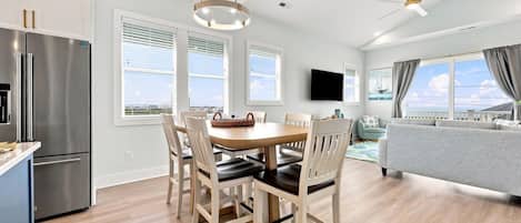 A modern kitchen with a dining area, a flat-screen TV, and a view of the sea.