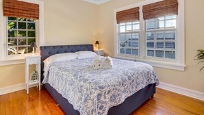Ein Schlafzimmer mit einem großen Bett, zwei Nachttischen und Fenstern mit Jalousien.