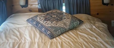 Un plafond en bois et un lit agrémenté d’un coussin à motifs.