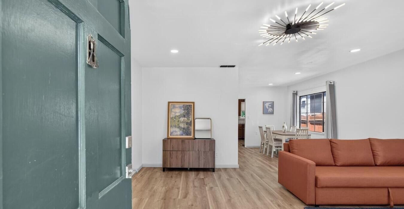 A modern interior with a wooden floor, a brown sofa, a dining area, and a ceiling light fixture.