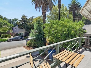 Ein Balkon mit Holzbank, Metallgeländer und Blick auf eine Straße mit parkenden Autos und einem Haus.