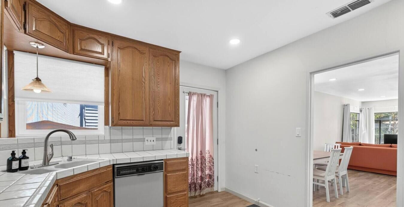 A kitchen with wooden cabinets, a dishwasher, and a window with blinds.
