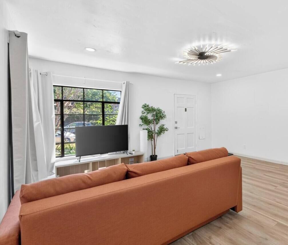 A modern living room with a sofa, a television, a potted plant, and a window with curtains.