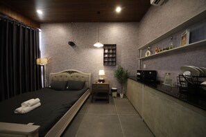 Un dormitorio con cama, mesita de noche, lámpara y una planta pequeña.