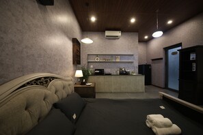 Ein Schlafzimmer mit Bett, Nachttisch, Lampe und einer kleinen Küchenzeile.