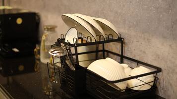 A kitchen counter with a dish rack holding white plates and bowls, a black appliance, and a jar with a spoon.