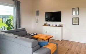 A modern living room with a grey sofa, a wooden coffee table, a TV mounted on the wall, and a cabinet with books and decorative items. - 1 bedroom stunning home in Kolobrzeg (Kolobrzeg)