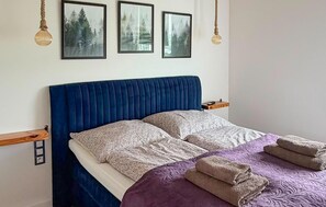 Ein Bett mit blauer Kopfteil, zwei Kissen, einer violetten Decke und zwei gefalteten Handtüchern.