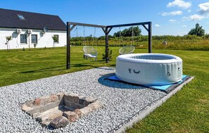 Ein Whirlpool auf einer Schotterterrasse mit einer hölzernen Pergola darüber, umgeben von einer Rasenfläche und einem Gebäude mit Fenstern und einer Satellitenschüssel.