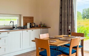 Une cuisine dotée d’un plan de travail en bois, de meubles blancs et d’un coin repas avec une table en bois et des chaises rembourrées bleues.