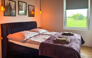 Ein Schlafzimmer mit einem Bett, einem Fenster mit Blick auf Grünflächen und drei gerahmten Bildern an der Wand.