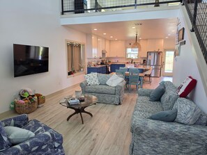 Ein geräumiges Wohnzimmer mit einem Flachbildfernseher, zwei Sofas, einem Couchtisch und einem Essbereich mit einer Küche im Hintergrund.