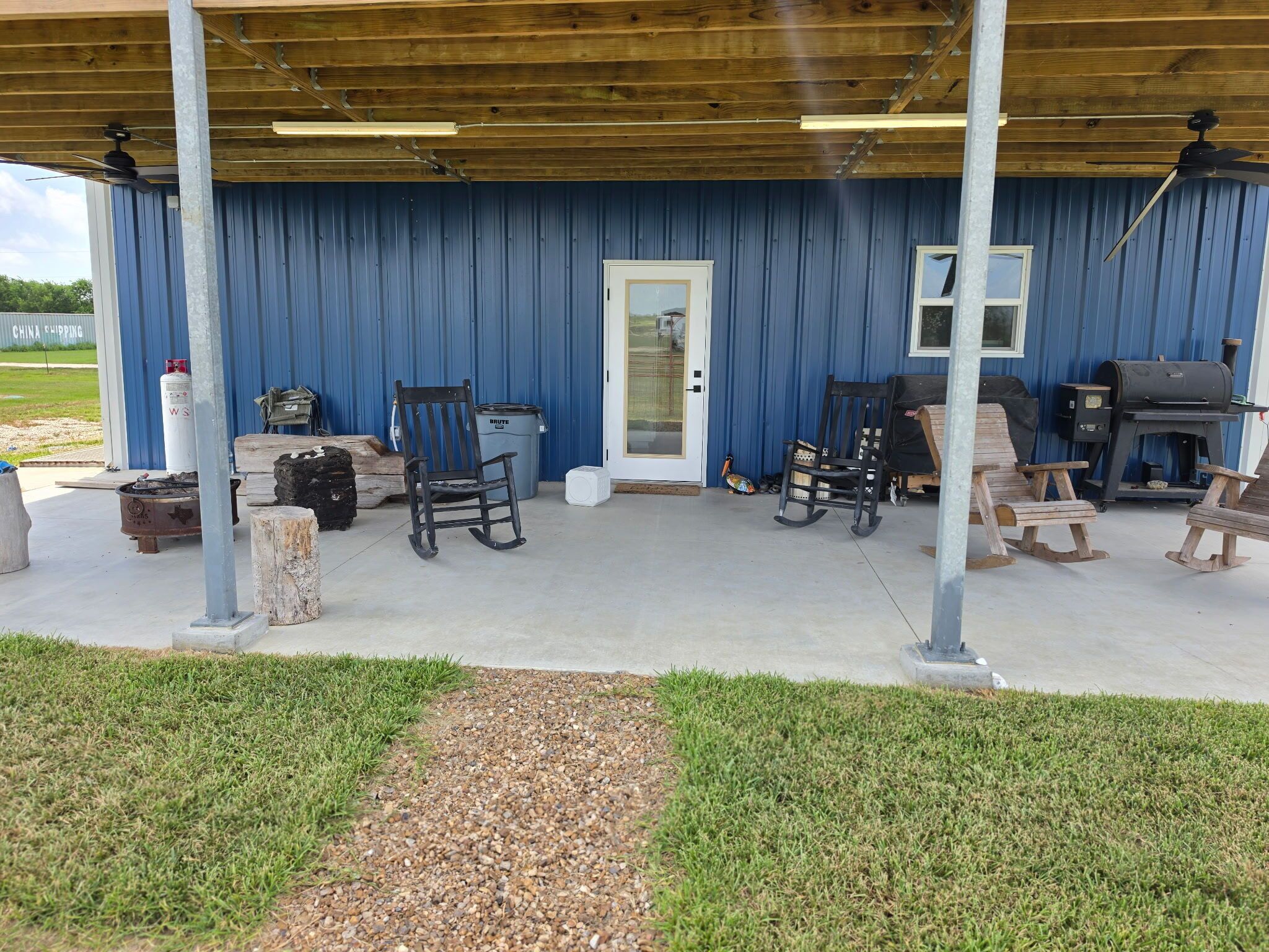 An outdoor covered patio area with seating, a barbecue grill, and a door leading to a building.