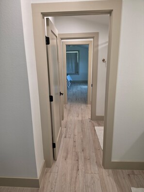 Ein Flur mit Holzdielen und weißen Wänden, der zu einem Zimmer mit Bett und Fenster führt.