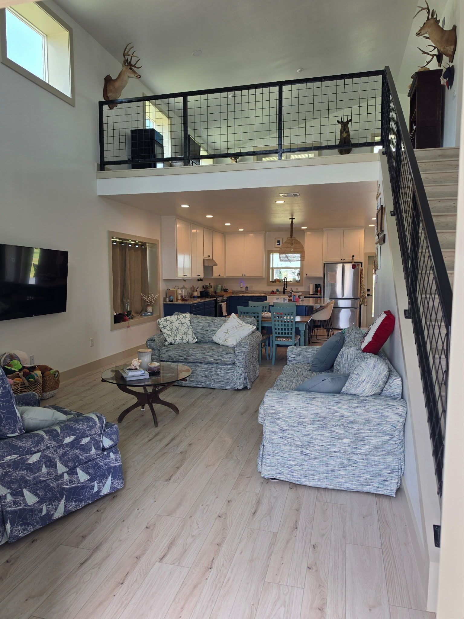 A spacious living area with a high ceiling, a kitchen in the background, and a staircase leading to an upper level.