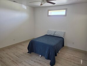 Ein Schlafzimmer mit einem Bett, einem Deckenventilator, einem Fenster und einem Lichtschalter an der Wand.