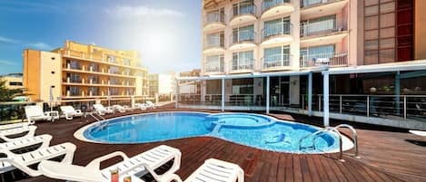 A rooftop swimming pool with lounge chairs and a building with balconies.