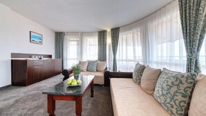A living room with a sofa, a coffee table with fruit, a cabinet, and sheer curtains. - Hotel Sveti Nikolai (Primorsko)