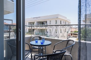 A balcony with a table and chairs, overlooking a building with a sign that reads 'Demokratias Court Tel.' - Modern 2BR Apt in Oroklini Larnaca (Voroklini)