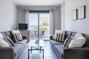 A modern living room with two grey sofas, a glass coffee table, and a TV on a stand. - Modern 2BR Apt in Oroklini Larnaca (Voroklini)