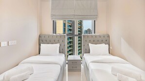 Ein Hotelzimmer mit zwei Betten, einem Fenster mit Blick auf Gebäude und einem kleinen Nachttisch.
