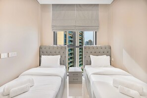 A hotel room with two beds, a window with a view of buildings, and a small bedside table. - Stylish 2BR with Canal Views in Business Bay (Dubai)