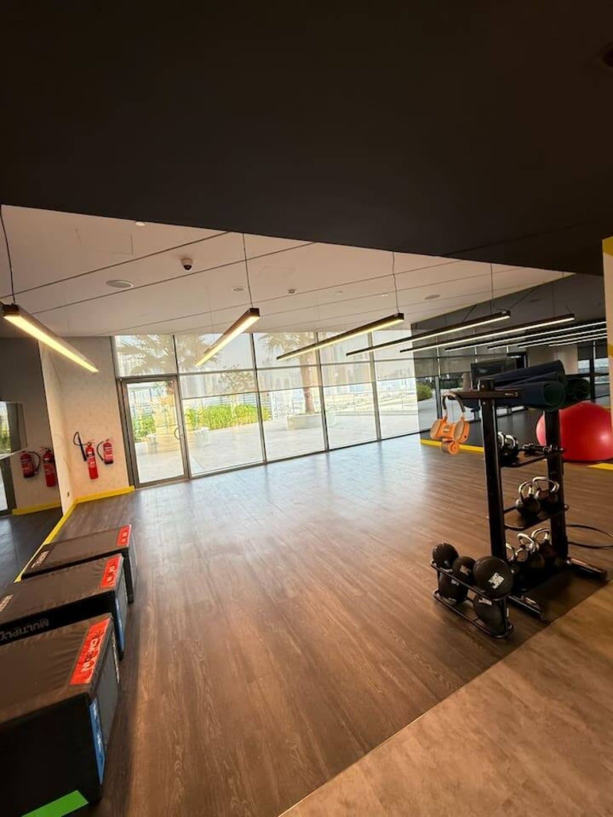 A gym with exercise equipment, large windows, and a wooden floor.
