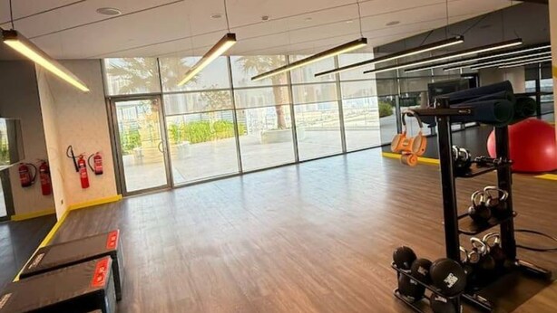 Ein Fitnessstudio mit Trainingsgeräten, großen Fenstern und Holzboden.