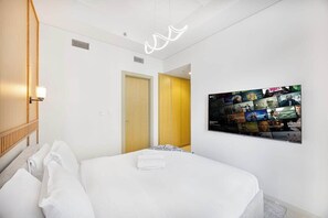 A hotel room with a neatly made bed, a wall-mounted TV displaying movie posters, and a modern light fixture. - Skyline View Apt in Business Bay w/Pool & Sauna (Dubai)
