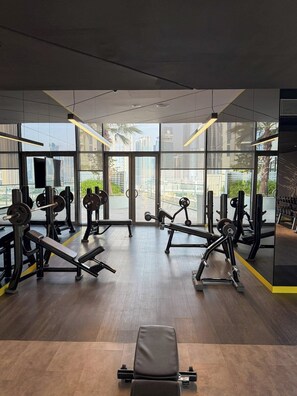 A gym with exercise equipment, large windows, and a view of the city. - Skyline View Apt in Business Bay w/Pool & Sauna (Dubai)