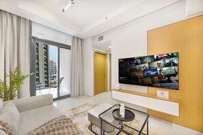 A modern living room with a large flat-screen TV displaying movie posters, a sofa, a coffee table, and a view of a cityscape through large windows. - Skyline View Apt in Business Bay w/Pool & Sauna (Dubai)